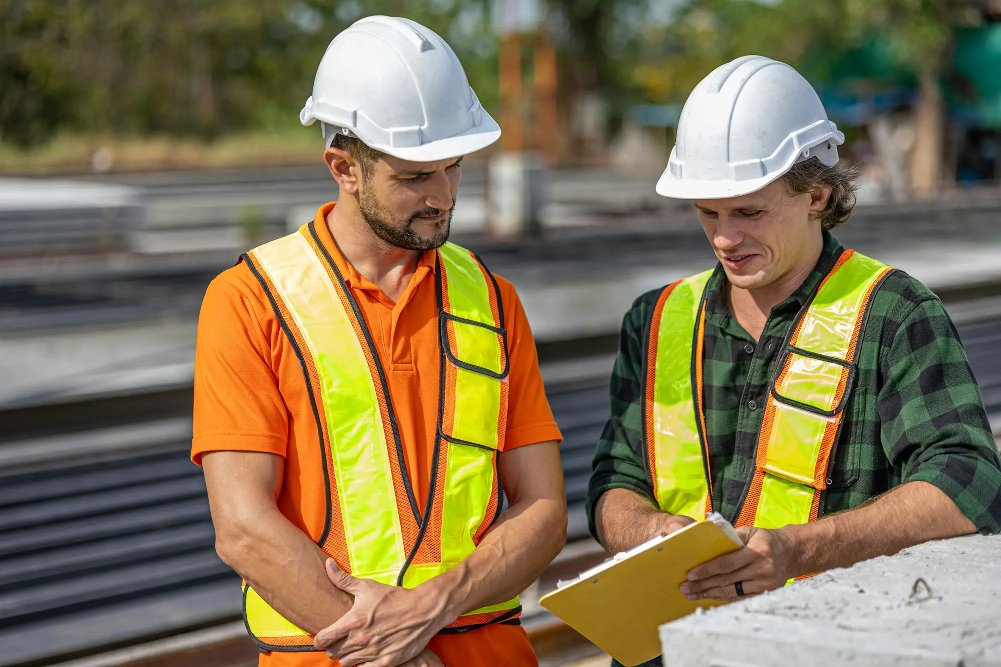 Site engineers in safety gear reviewing plans beside railway tracks